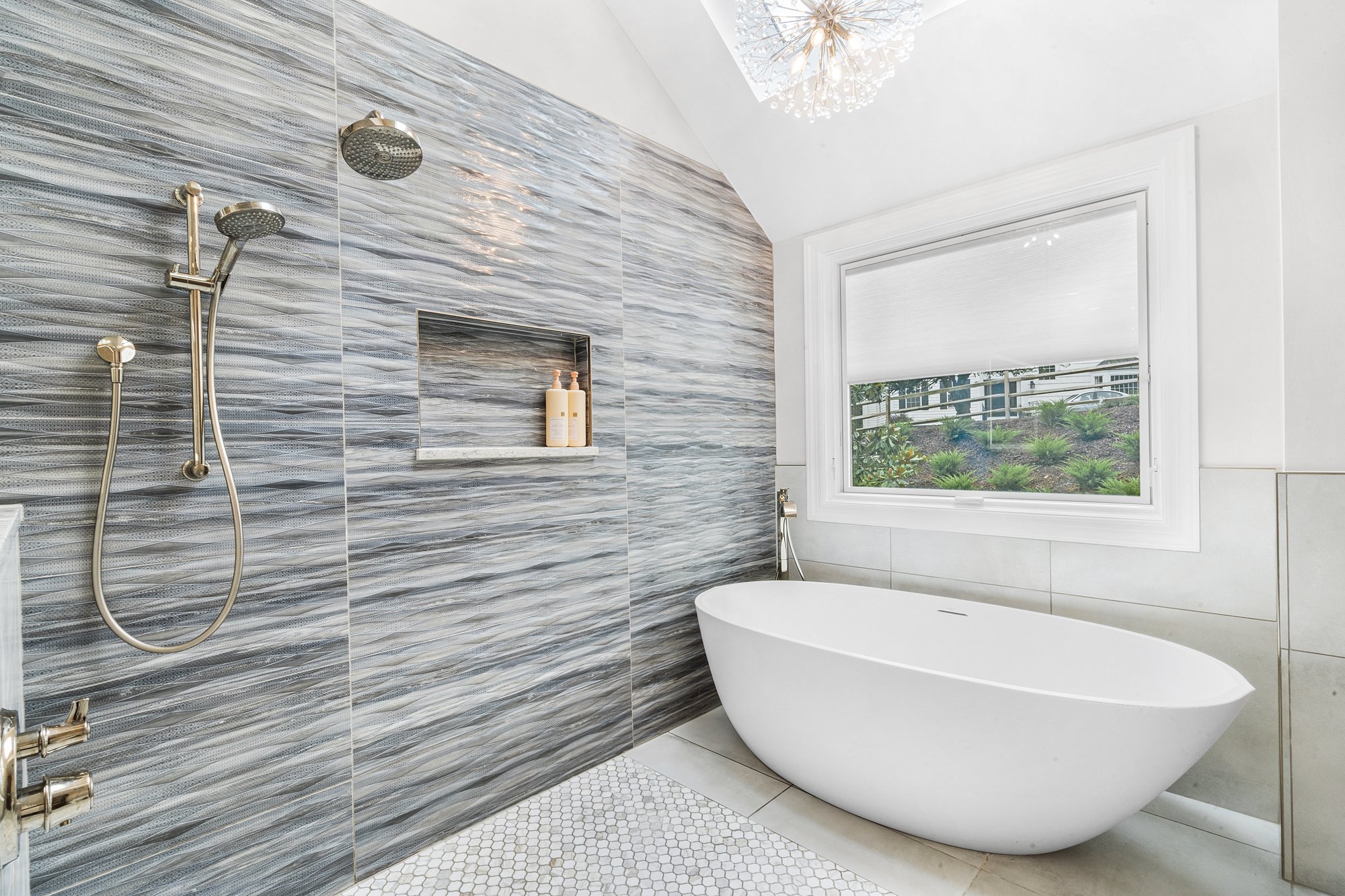 Freestanding tub against a gray wall with a built-in shower niche, creating an open and modern bathroom design