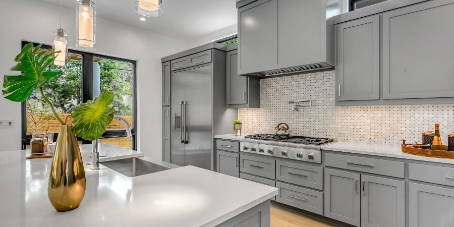 Contemporary kitchen with sleek white countertop and gray cabinets and appliances behind it.