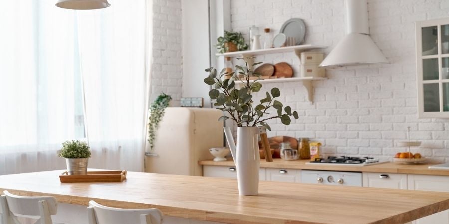 Kitchen table with plants on top, with a white brick backsplash and white appliances and shelves behind it.