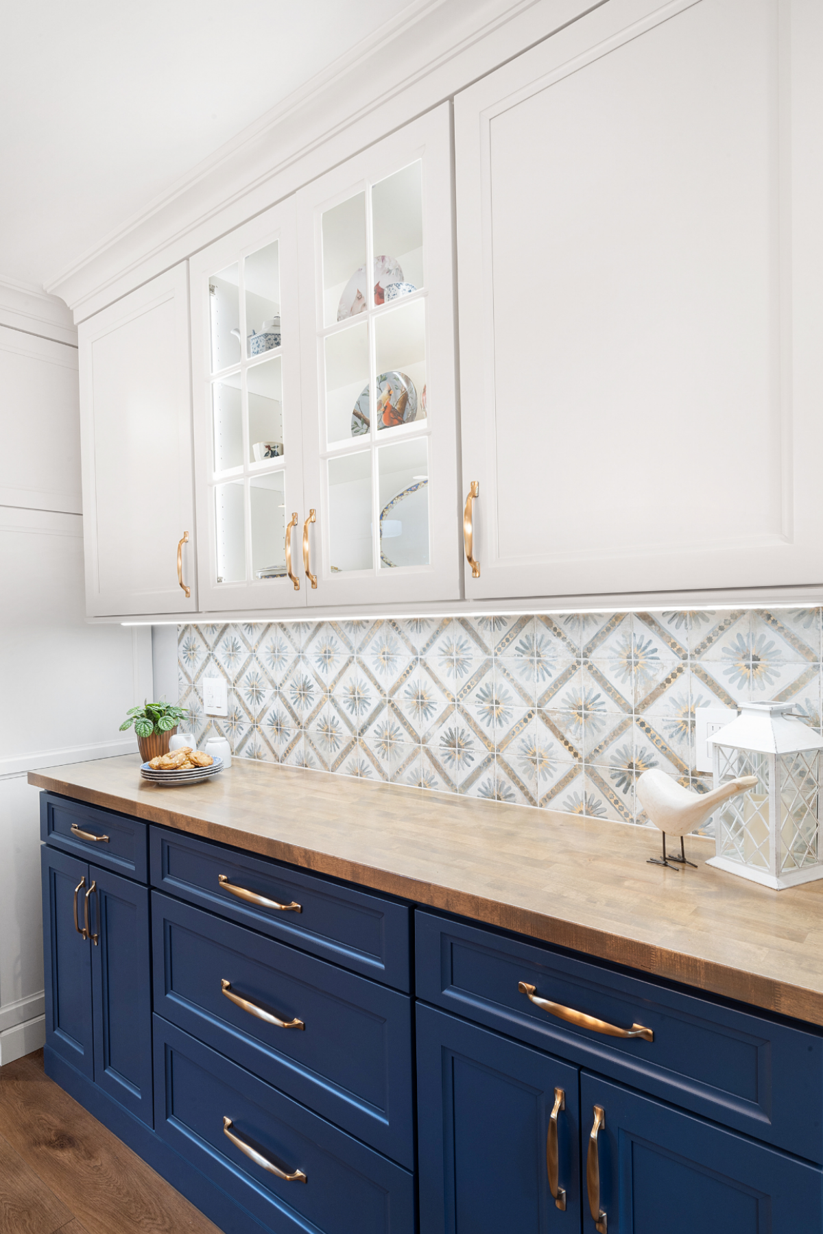 Blue shaker cabinets with custom glass cabinetry above, butcher block-style countertops, and a patterned tile backsplash for a stylish, layered kitchen design. Blue shaker cabinets with custom glass cabinetry above, butcher block-style countertops, and a patterned tile backsplash for a stylish, layered kitchen design.