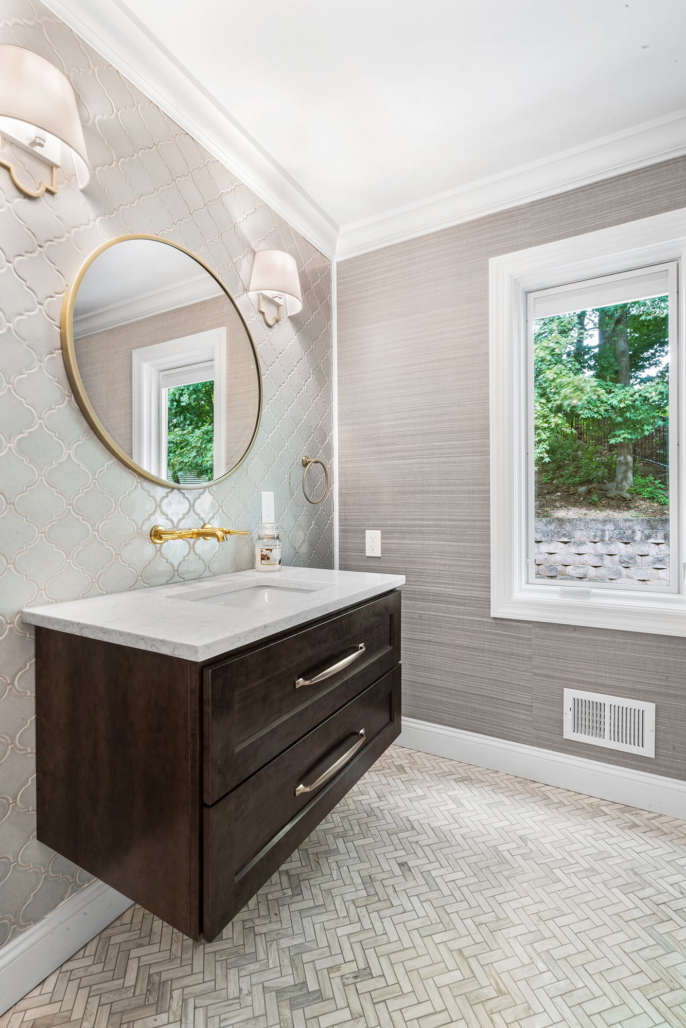 Powder room with floating vanity and herringbone tile pattern flooring, complimented by gold accents.