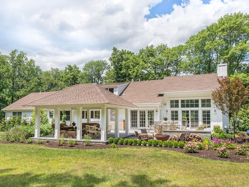 Exterior custom pavilion remodel with white custom traditional paneled columns on blue stone patio with garden and Andersen windows on home in Boonton, New Jersey renovated by JMC Home Improvement Specialists