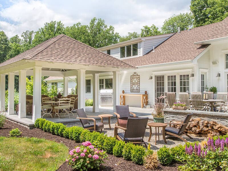 Custom pavilion remodel with white custom traditional paneled columns on blue stone patio with garden, fire pit and outside dining area with Andersen windows and doors on home in Boonton, New Jersey renovated by JMC Home Improvement Specialists