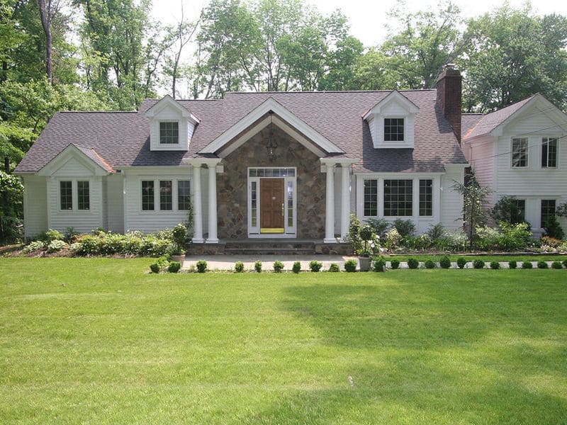 Exterior home remodel with Andersen front door with side lights and transom windows, round columns and stone front, cape cod dormers in Mountain Lakes, New Jersey renovated by JMC Home Improvement Specialists