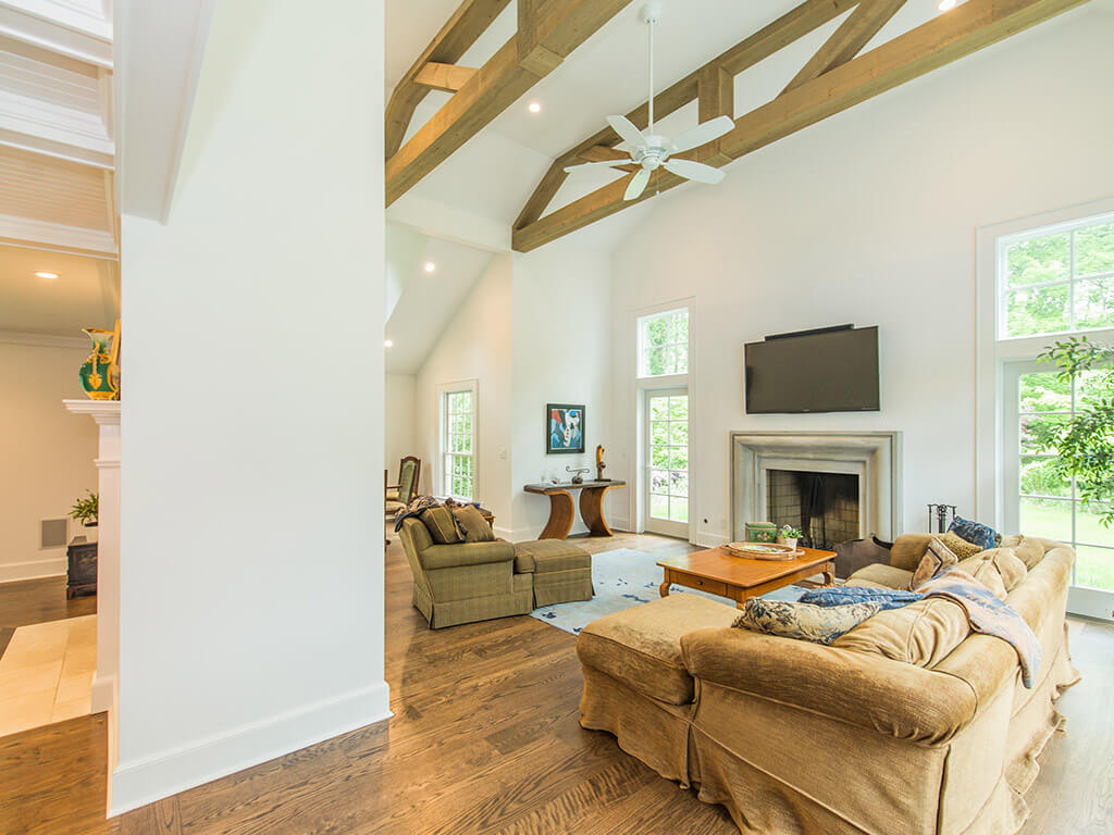 Rustic Family room remodel with TV over Old world cement mantel with 7” oak plank flooring and vaulted ceiling with ceiling fans and wood beams in Morris County, New Jersey renovated by JMC Home Improvement Specialists