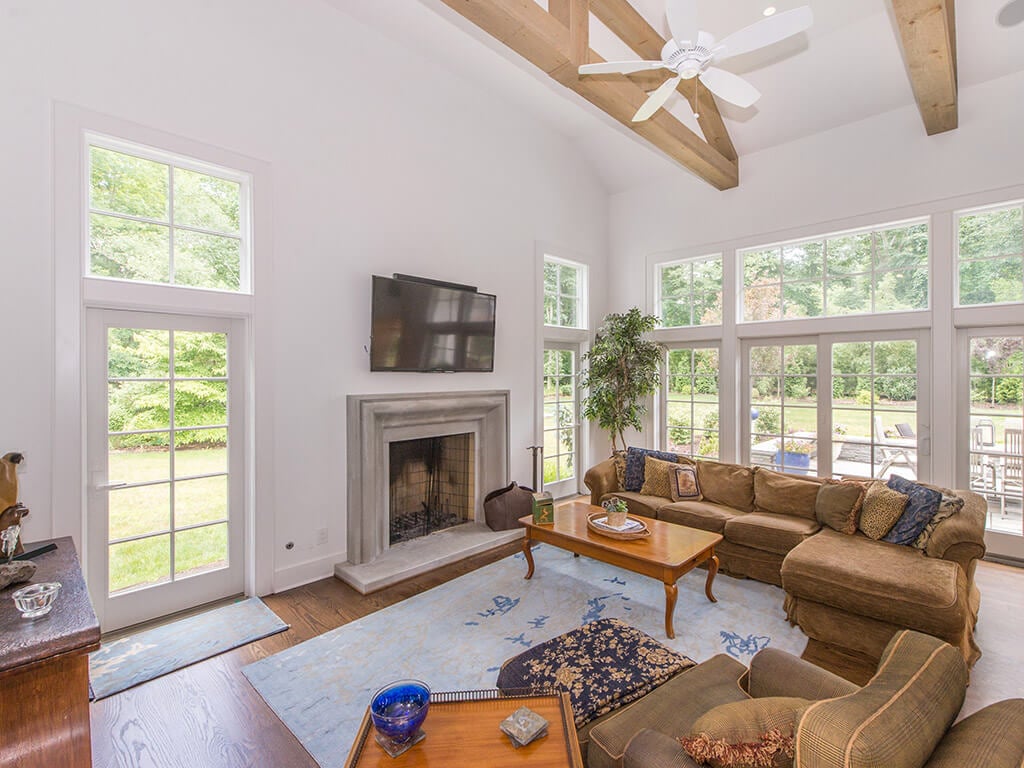 Rustic family room with old-world cement mantel on fireplace with TV above, 7 inch oak plank flooring, and Andersen doors and windows in Morris County, NJ renovated by JMC Home Improvement Specialists