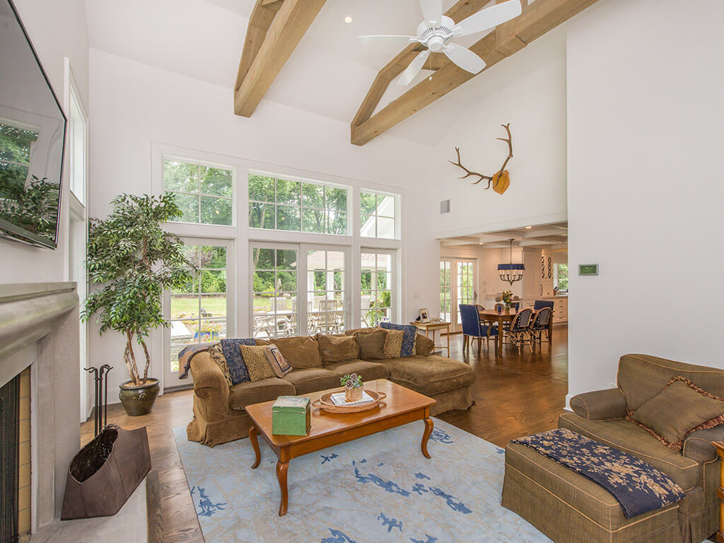 Corner view rustic Family room remodel with 7” oak plank flooring, vaulted ceiling with ceiling fans, reclaimed wood beams and Andersen windows in Boonton, NJ renovated by JMC Home Improvement Specialists