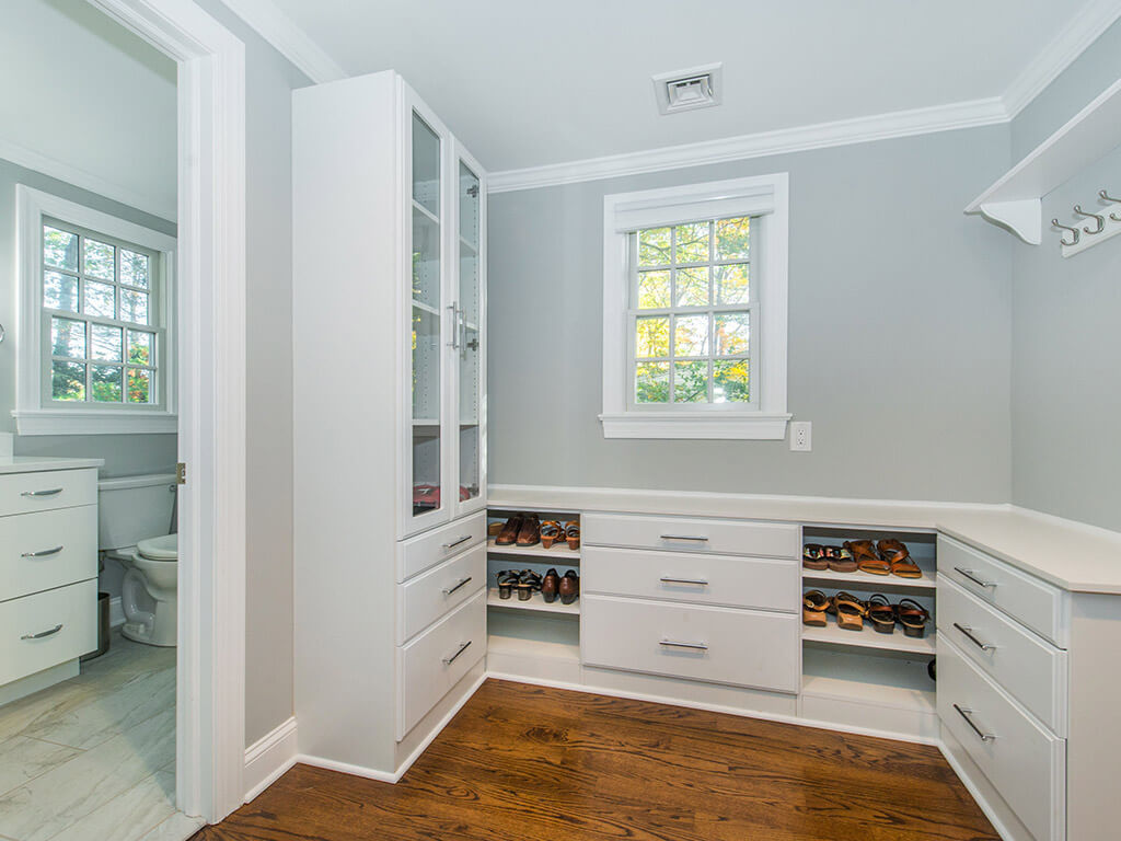 Custom white master bedroom walk-in closet with shelving and drawers, hardwood floor and entrance to master bathroom In Springfield, New Jersey renovated by JMC Home Improvement Specialists