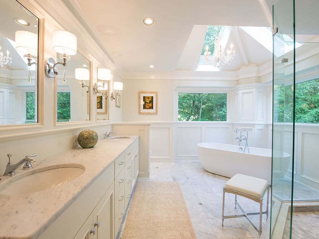 Dual white vanity with triple mirror and sconces with Carrera marble, wainscoting with soaking tub in Sparta, NJ Renovated by JMC Home Improvement Specialists