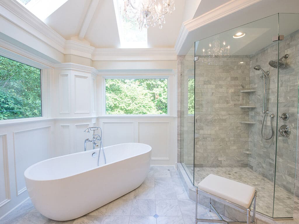 White master bath Vaulted Ceiling with skylight, wainscoting, paneling freestanding soaking tub with walk-in shower with dual shower heads and frameless glass and Carrera marble in Sparta, NJ Renovated by JMC Home Improvement Specialists