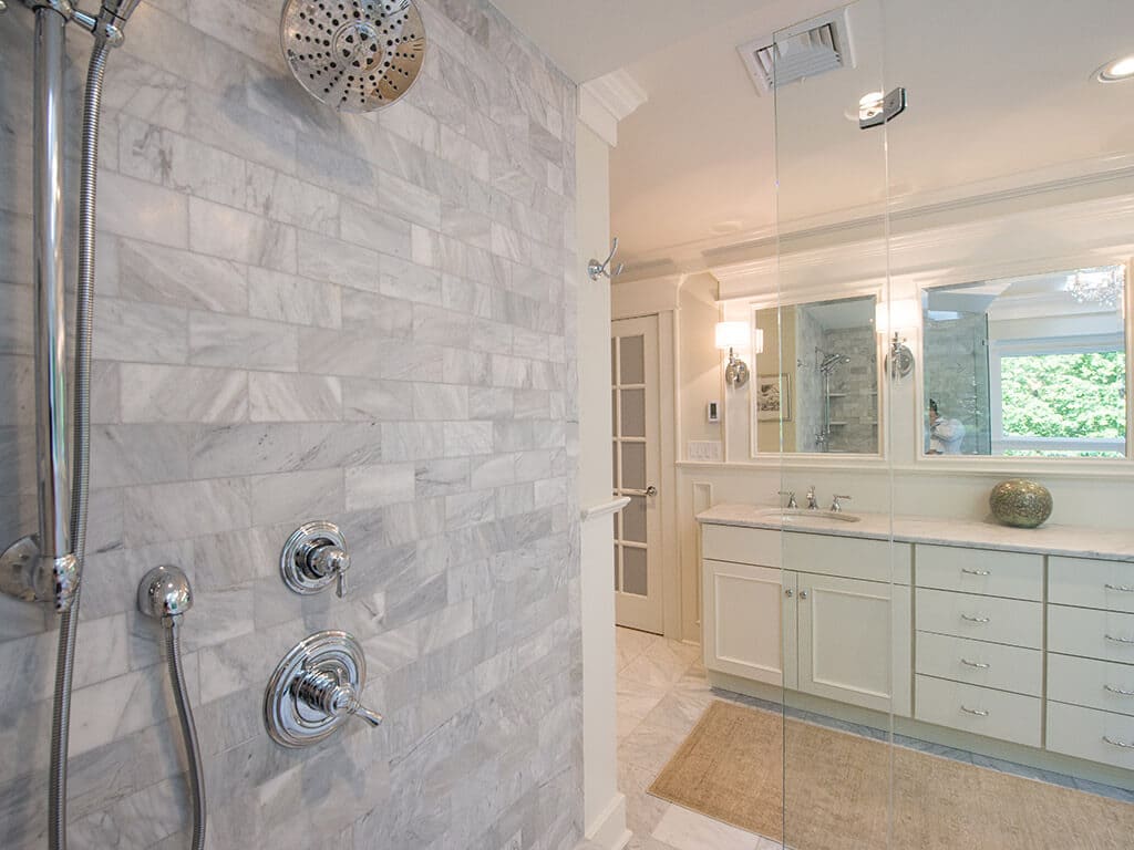 Inside walk-in shower with dual shower heads and frameless glass and Carrera marble with white vanity in Sparta, NJ Renovated by JMC Home Improvement Specialists