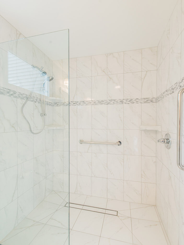 White handicap bathroom remodel with mosaic tile with accent stripe in roll-in shower with linear shower drain and glass panel in Mount Tabor, NJ renovated by JMC Home Improvement Specialists
