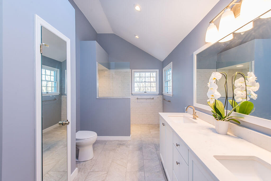 Master bathroom remodel in Chatham, NJ with linen closet and dual white marble countertop with framed mirror and walk-in shower with half wall and glass panel renovated by JMC Home Improvement Specialists