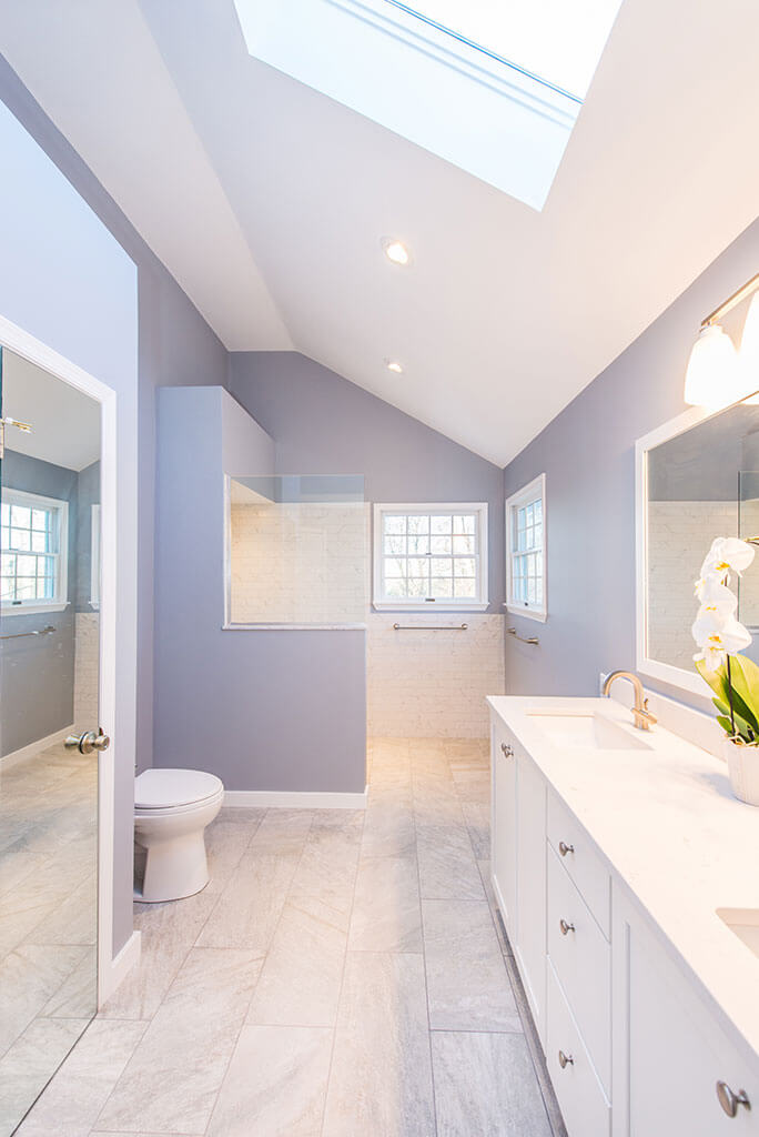 Chatham, NJ master bathroom remodel with skylight, linen closet and dual white vanity with marble countertop and framed mirror,  walk-in shower with half wall and glass panel renovated by JMC Home Improvement Specialists