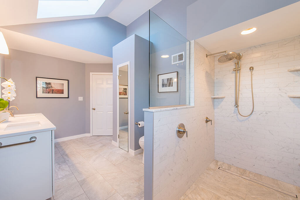 Master bathroom remodel with skylight, linen closet and dual white vanity with marble countertop and framed mirror,  walk-in shower with half wall and glass panel renovated by JMC Home Improvement Specialists in Chatham, NJ