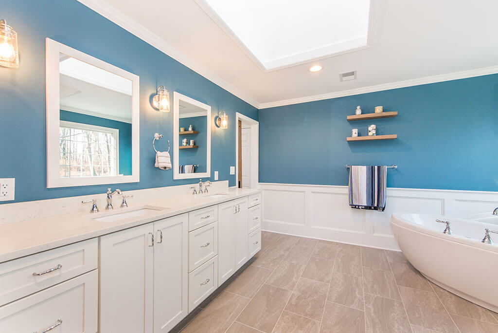 Master bathroom remodel soaking tub, white wall paneling, blue painted, wood like tile floor, white shaker his and hers vanity with quartz counters in Chester, NJ renovated by JMC Home Improvement Specialists