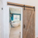 Barn door to master bathroom remodel with white wall paneling, blue painted walls, freestanding soaking tub and wood like tile floor in Chester, NJ renovated by JMC Home Improvement Specialists