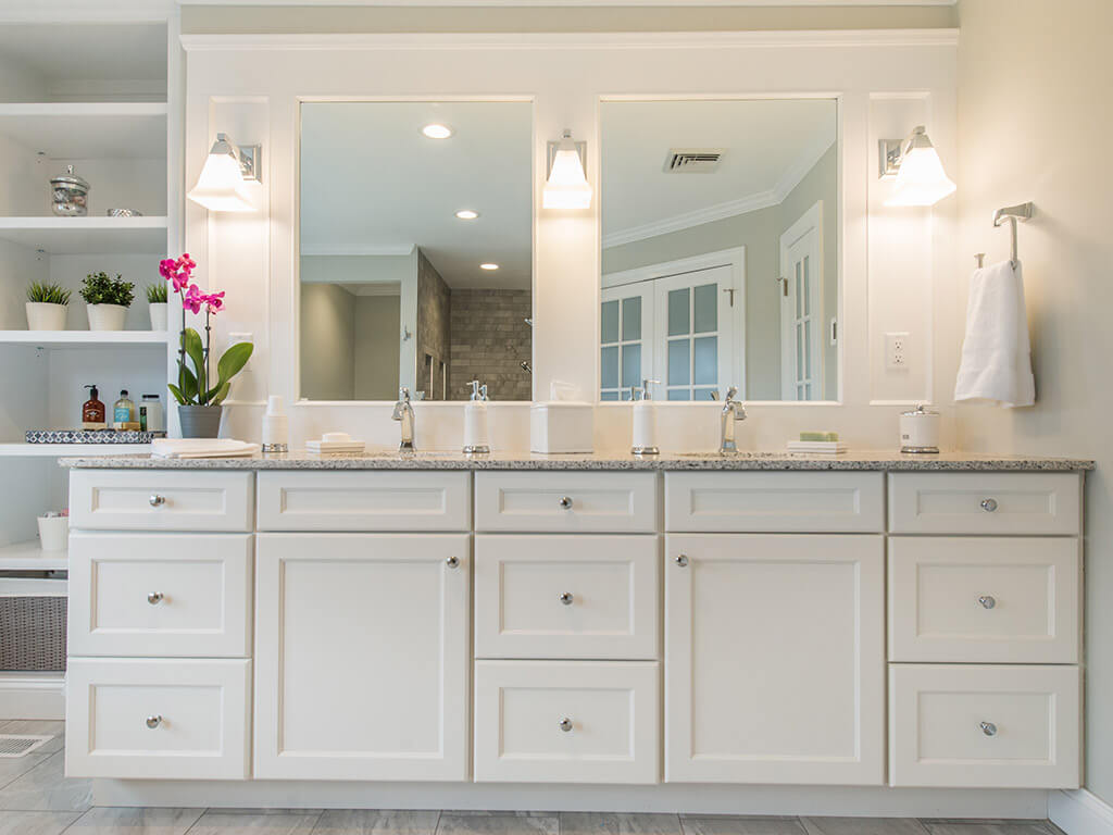 White shaker cabinet vanity with dual sink quartz countertop, sconces and custom trim around mirrors with built-in bookcase in Green Township, NJ renovated by JMC Home Improvement Specialists 