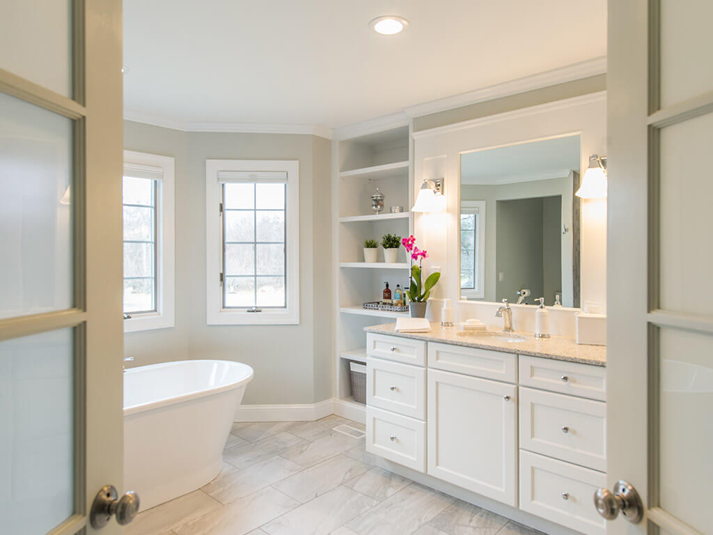 French door entrance to elegant white master bathroom with soaking tub and large floor tile with white shaker vanity with quartz counter top in Green Township, NJ renovated by JMC Home Improvement Specialists 