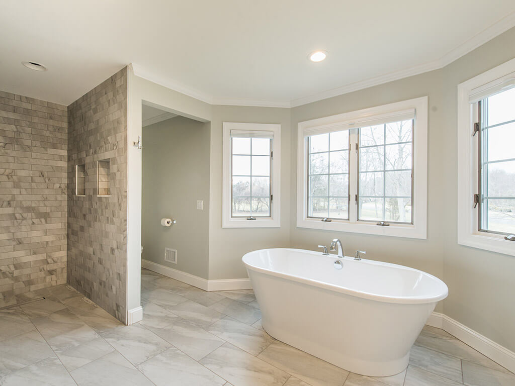 Elegant master bathroom remodel with large floor tile, roll-in shower with linear shower drain, toilet room and soaking tub surrounded by Andersen windows with white trim Morris County, NJ renovated by JMC Home Improvement Specialists 