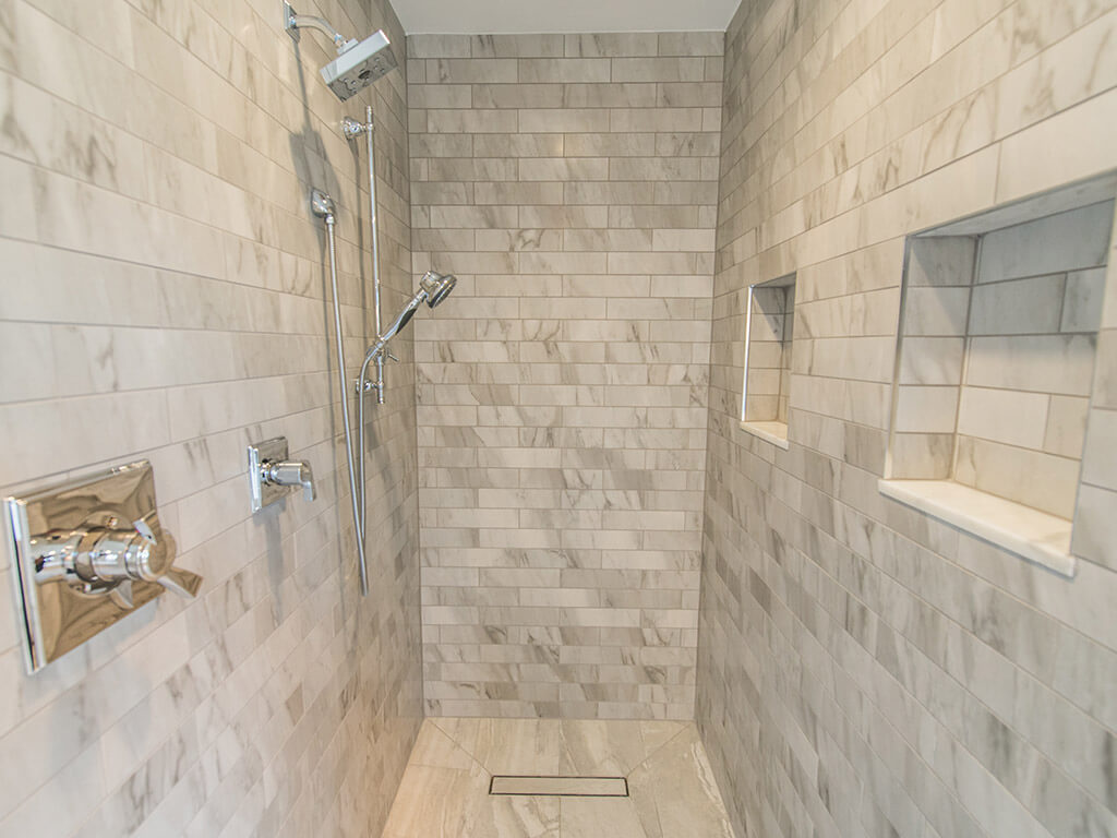 Gray tile roll-in shower with linear shower drain, niches with dual shower heads in Morris County, NJ renovated by JMC Home Improvement Specialists 