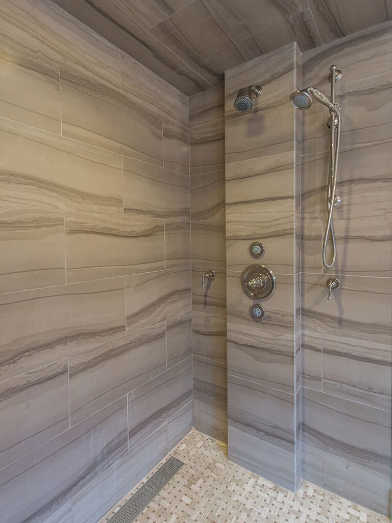 Master bathroom shower with stone walls and dual shower heads with monochromatic taupe, and basket weave tile floor in Boonton, NJ renovated by JMC Home Improvement Specialists