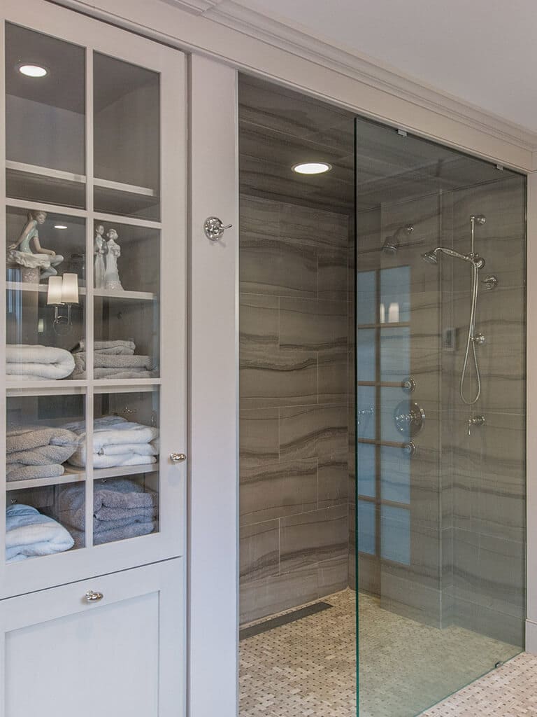 Master bathroom remodel with clear glass shower door panel to walk-in shower with linear drain, stone wall tile, custom inset linen with pullout hamper in monochromatic taupe in Boonton, NJ renovated by JMC Home Improvement Specialists