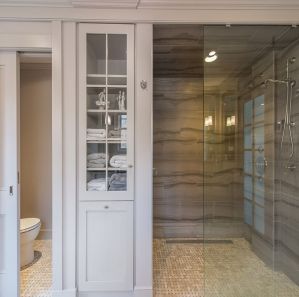 Award winning monochromatic taupe bathroom remodel with clear glass shower door panel to walk-in shower with linear drain, stone wall tile, custom inset linen with pullout hamper, pocket door to separate toilet room, heated basketweave floor in Boonton, NJ renovated by JMC Home Improvement Specialists