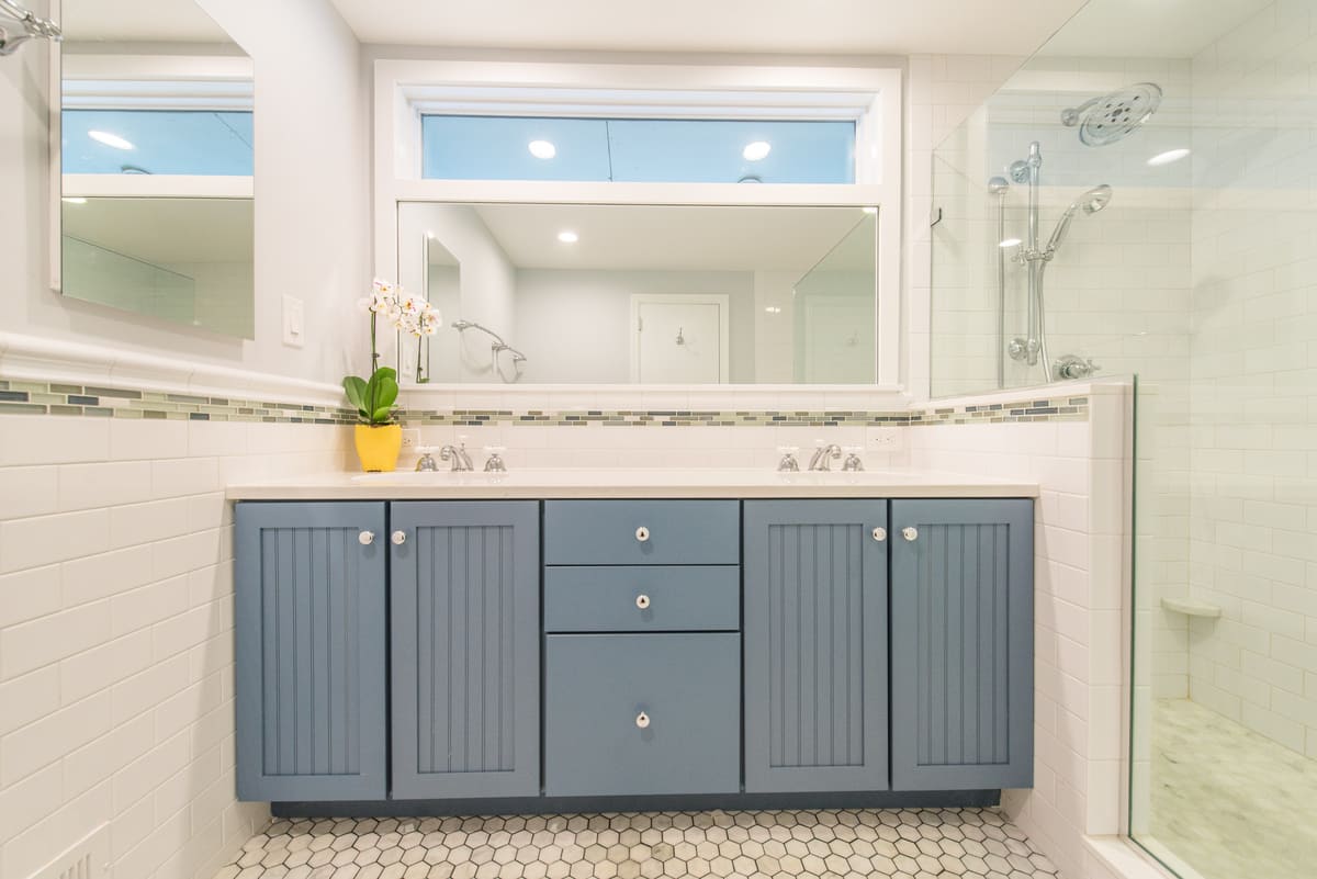 Lake House bathroom remodel with blue painted vanity with quartz countertop, marble octagon floor and white subway tile with glass strip on wall, transom window with white trim above mirror, medicine cabinet and clear glass panel walk-in shower in Morris County, NJ renovated by JMC Home Improvement Specialists