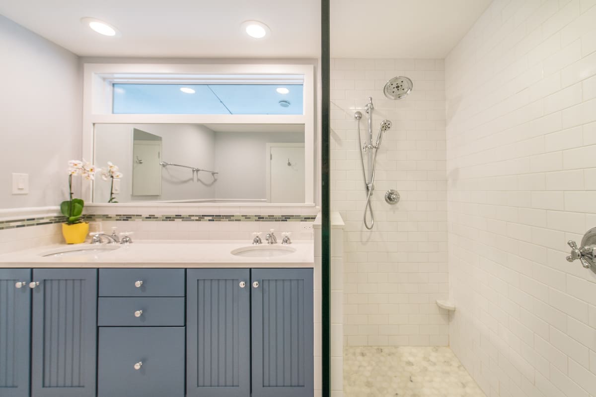 Lake House bathroom remodel with custom blue painted vanity with quartz countertop, marble octagon floor and white subway tile with glass strip on wall, transom window with white trim above mirror, medicine cabinet and clear glass panel walk-in shower with chrome finishes in Lake Hopatcong, NJ renovated by JMC Home Improvement Specialists