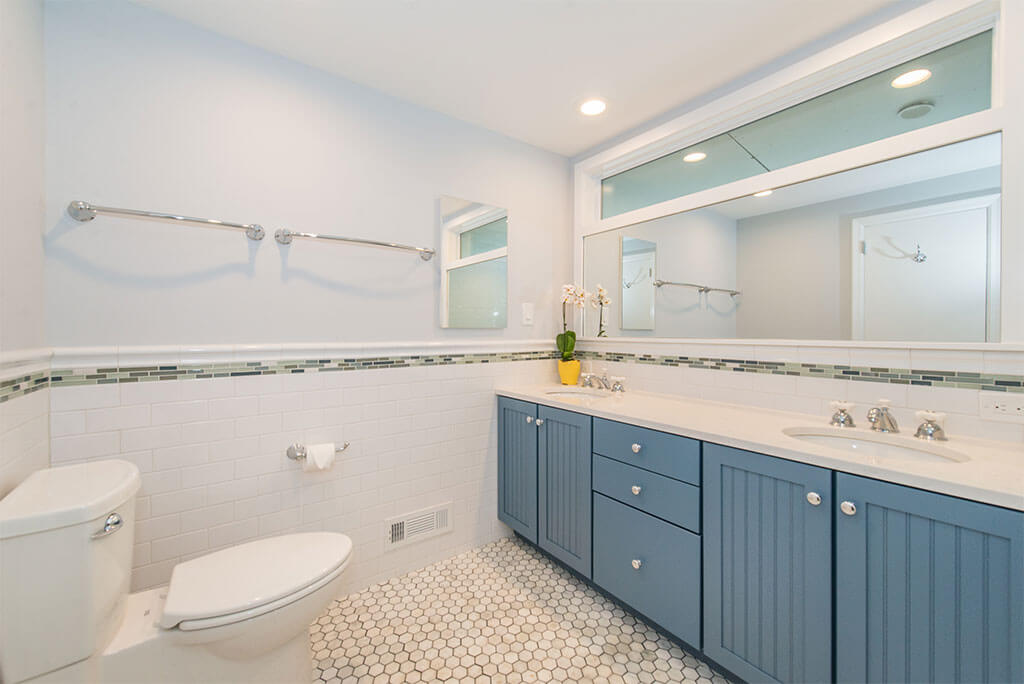 Blue painted vanity with quartz countertop, marble octagon floor and white subway tile with glass strip on wall, transom window with white trim above mirror in Lake Hopatcong, NJ remodeled by JMC Home Improvement Specialists