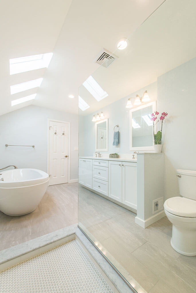 White master bathroom remodel with vaulted ceilings, natural light, his and hers vanity, white framed mirrors, clear glass shower door panel, and soaking tub in Madison, NJ renovated by JMC Home Improvement Specialists