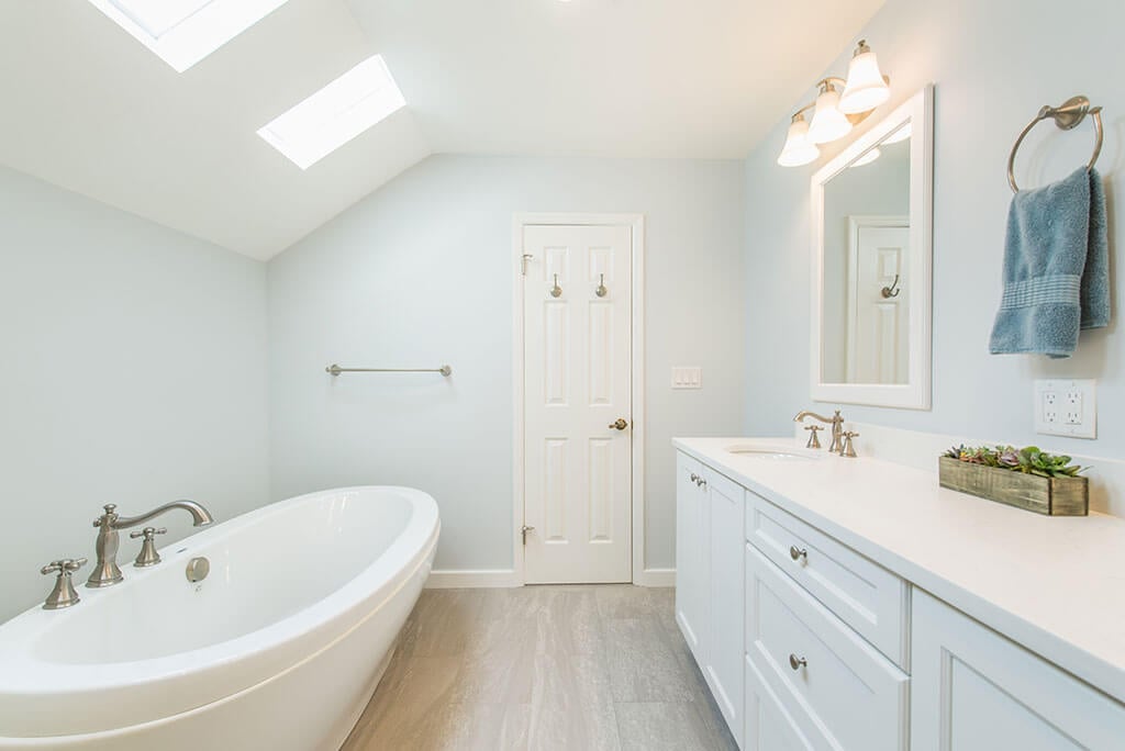 White master bathroom remodel with vaulted ceilings, skylight for natural light, his and hers vanity, white framed mirrors and soaking tub in Madison, NJ renovated by JMC Home Improvement Specialists