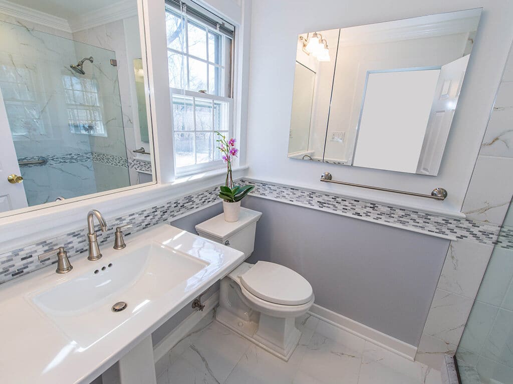 Small grey and white bathroom remodel with Kohler pedestal sink, built-in mirror, medicine cabinet, grey and white glass tile stripe accent and brushed nickel finishes in New Providence, NJ renovated by JMC Home Improvement Specialists