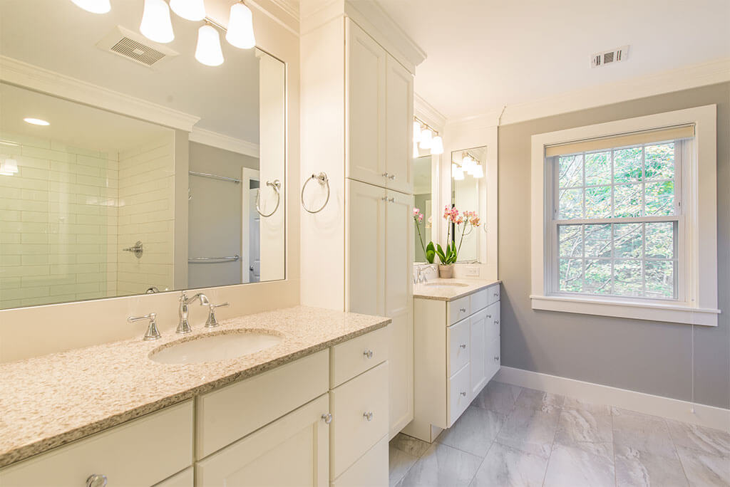 Master bathroom remodel with his and hers separate white vanities, quartz counters, linen cabinet and grey painted walls with white crown molding in Morristown, NJ renovated by JMC Home Improvement Specialists