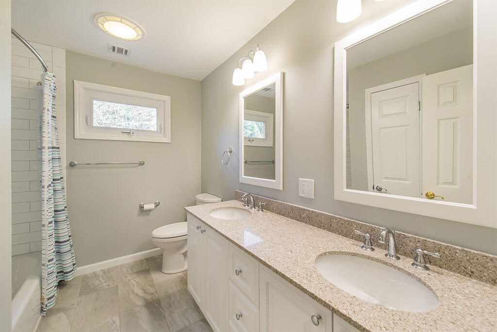 Hall bathroom remodel with his and hers white vanities, white framed mirrors, tub and curved curtain with white subway tile and grey painted walls  in Morristown, NJ renovated by JMC Home Improvement Specialists