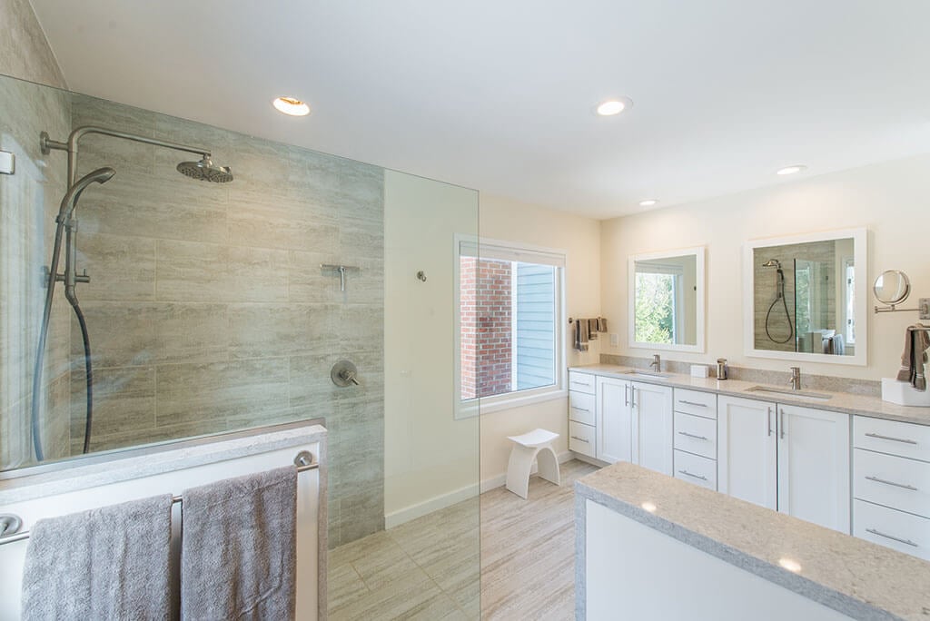 Master bathroom remodel with curbless, roll-in shower with frameless glass panel, Kohler hydro rail, half wall by toilet, white shaker his and hers vanity with quartz counters and white framed mirrors in Chester, NJ renovated by JMC Home Improvement Specialists