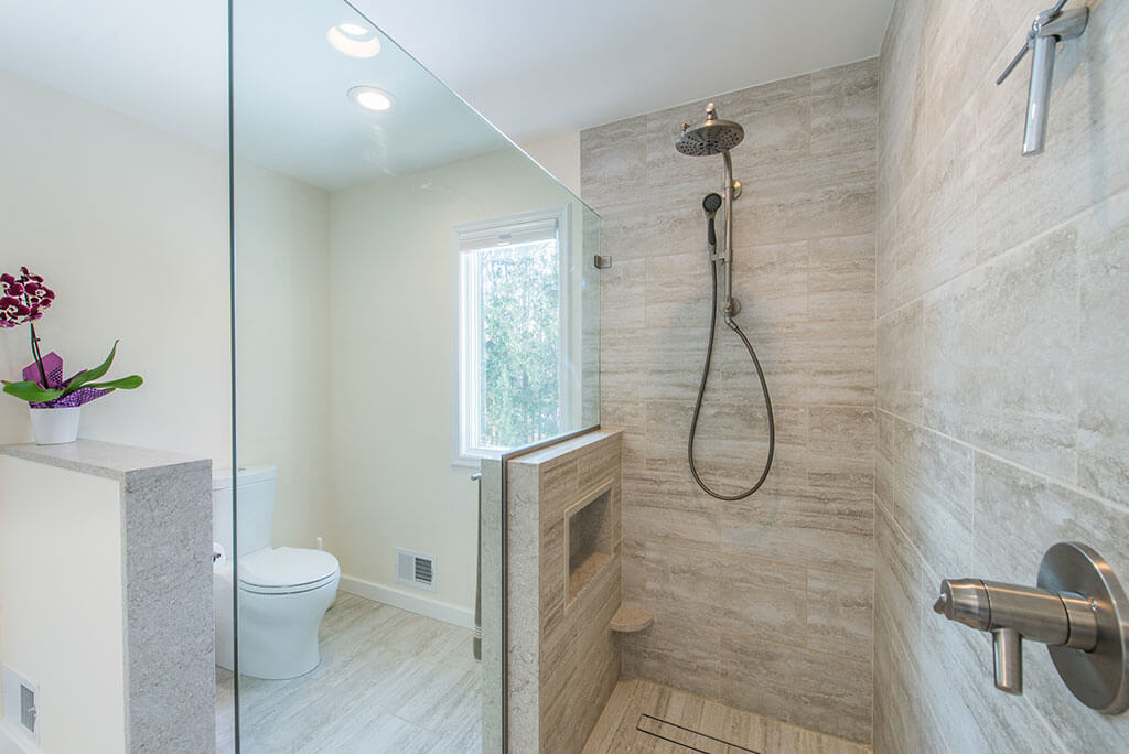 Master bathroom remodel with curbless, roll-in shower with frameless glass panel, Kohler hydro rail and skirted toilet in Chester, NJ renovated by JMC Home Improvement Specialists