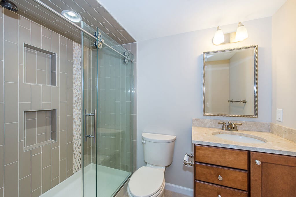 Hall bathroom remodel with clear glass shower door, double niche in shower with corner shelf, wood vanity with undermount sink in Morristown, NJ renovated by JMC Home Improvement Specialists
