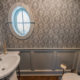 Powder room with wall panels, crown molding, retro pedestal sink with chrome legs, decorative white mirror, chandelier, Farrow & Ball paint and paper and oval window in Boonton, NJ renovated by JMC Home Improvement Specialists
