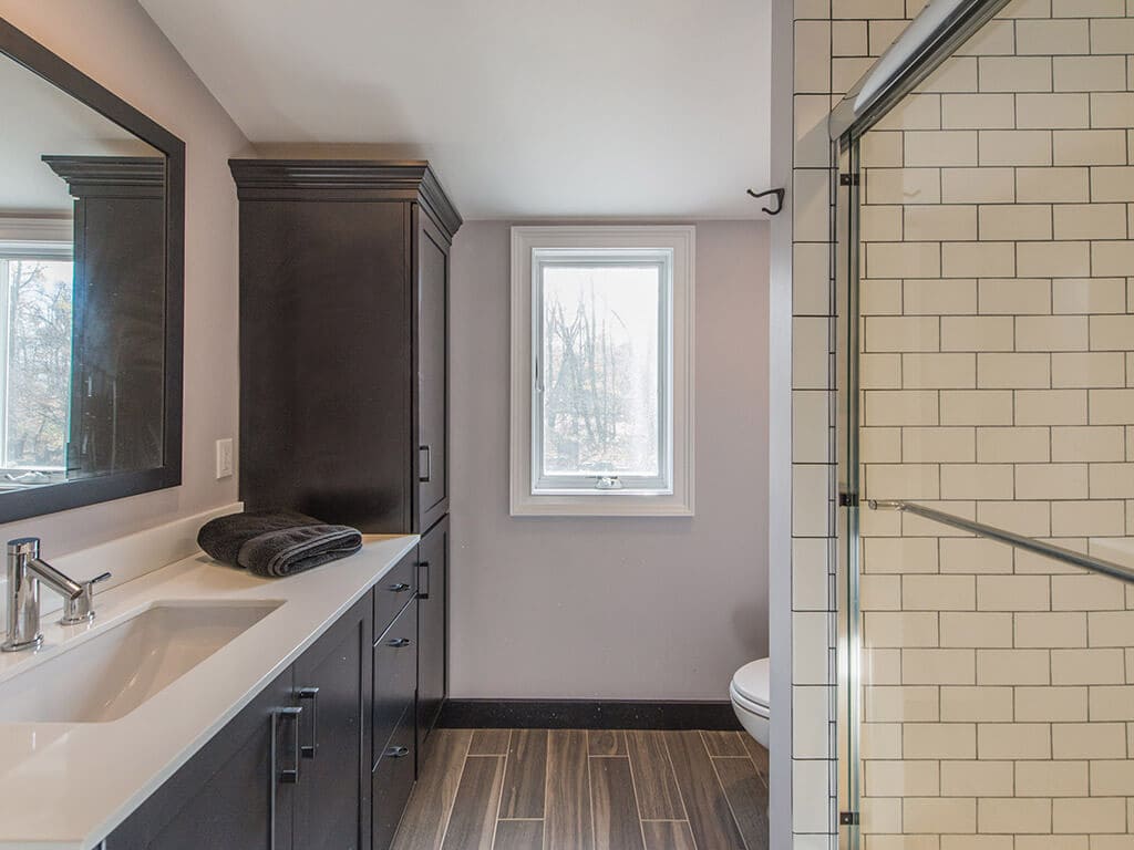 Bathroom remodel with wood like tile floor, black cabinets, linen cabinet, subway tile with grey grout in shower with chrome finishes in Boonton, NJ renovated by JMC Home Improvement Specialists