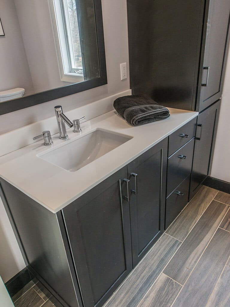 Bathroom remodel with wood like tile floor, black cabinets, linen cabinet, framed mirror, quartz counter with undermount sink with chrome finishes in Boonton, NJ renovated by JMC Home Improvement Specialists