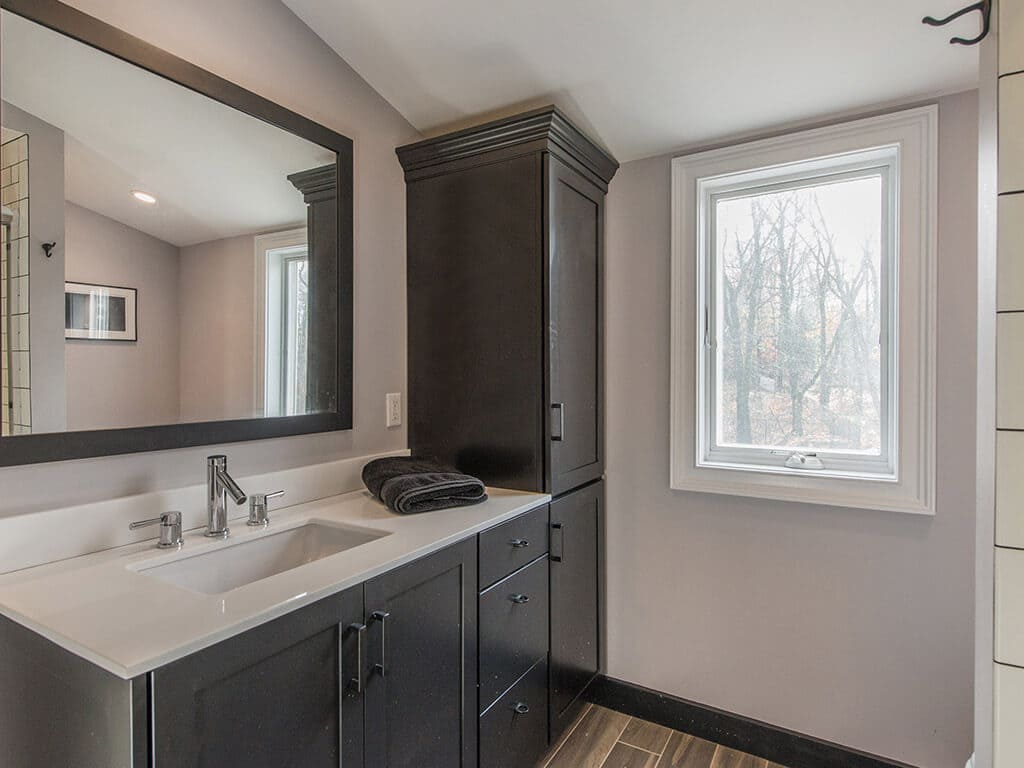 Bathroom remodel with wood like tile floor, black cabinets, linen cabinet, framed mirror, quartz counter with undermount sink with chrome finishes in Morris County, NJ renovated by JMC Home Improvement Specialists