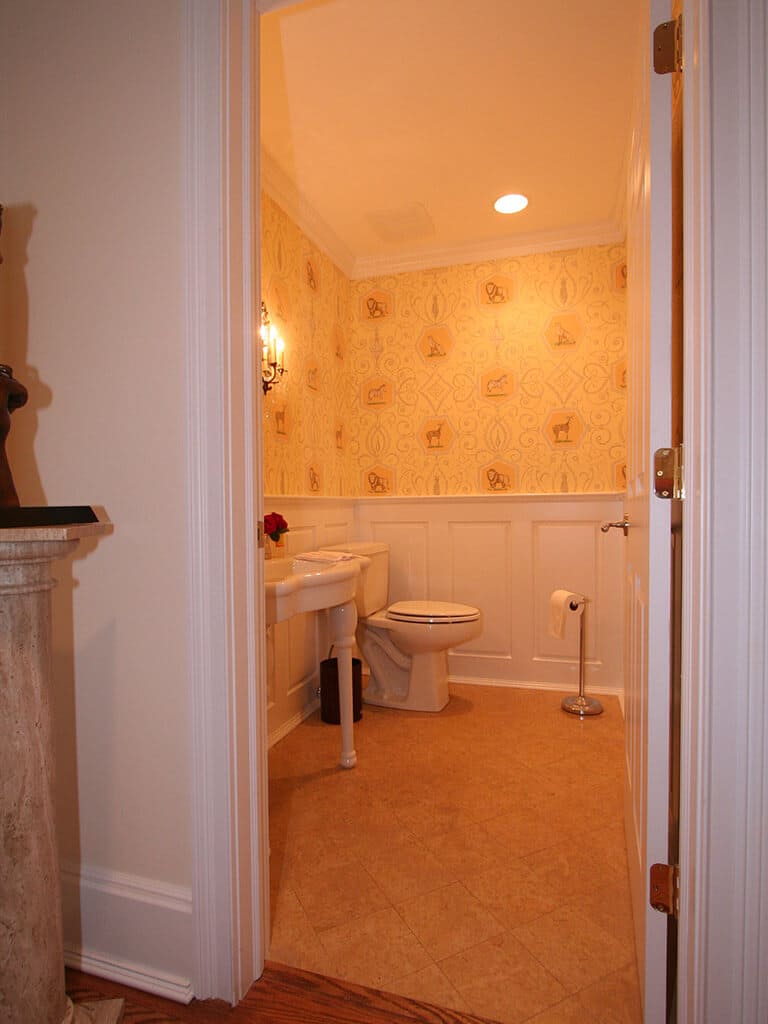 Powder room remodel with crown molding, white wall panel and decorative wall paper, pedestal sink and decorative mirror in Mountain Lakes, NJ renovated by JMC Home Improvement Specialists