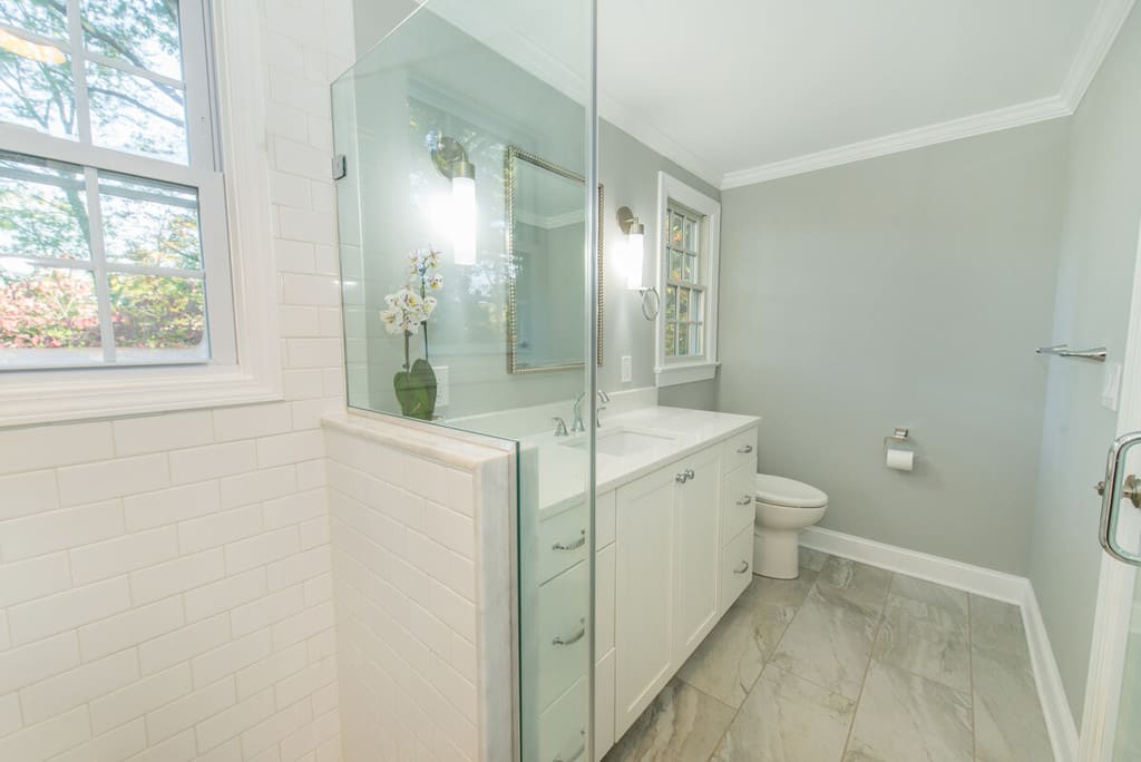 Bathroom remodel with white subway tiles in shower framing window with chrome finishes, white vanity with quartz counter and decorative framed mirror in Springfield, NJ renovated by JMC Home Improvement Specialists