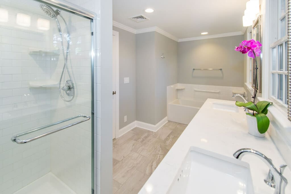 White bathroom remodel with chrome finishes and grey walls with white crown molding, dual white vanity, quartz counter, undermount sinks, shower with white subway tile, separate tub in Springfield, NJ renovated by JMC Home Improvement Specialists