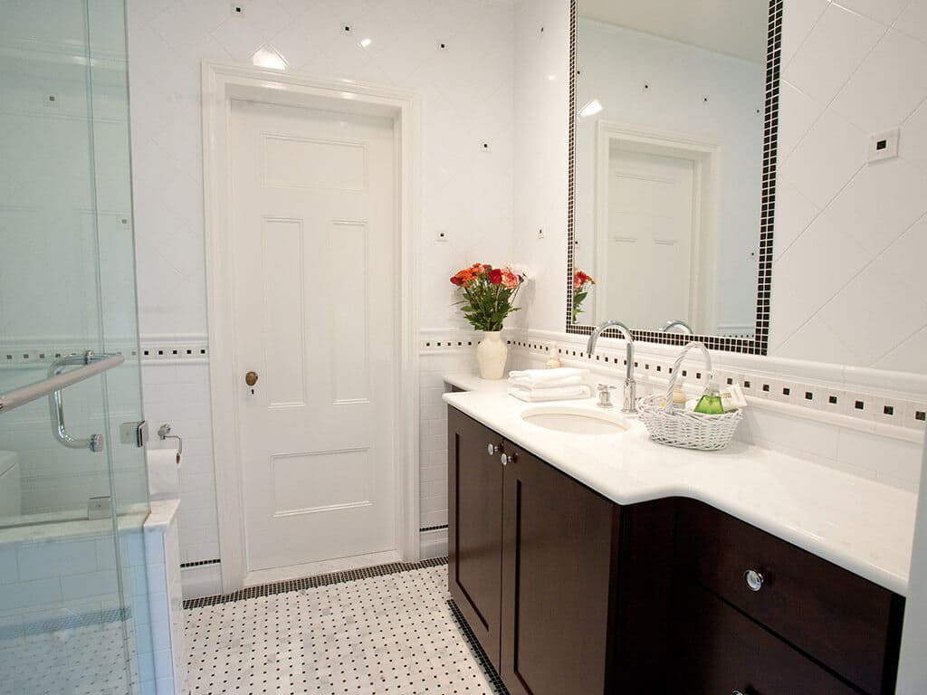 Black and white master bathroom remodel with espresso and marble vanity, tile around mirror, basketweave floor, Carrera tiles and clear glass panel shower door and chrome finishes in Morristown, NJ renovated by JMC Home Improvement Specialists