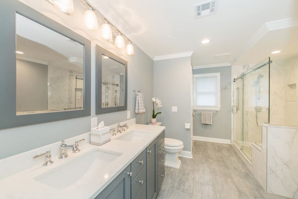 Grey and white bathroom remodel with dual undermount sink vanity with shaker cabinets, grey wood framed mirrors, frameless sliding shower door with Carrera marble in Randolph, NJ renovated by JMC Home Improvement Specialists