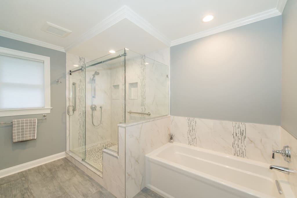 Grey and white master bathroom remodel with crown molding, Kohler accessories, frameless sliding shower door with Carrera marble, bench seat, niche, basketweave shower floor, separate soaking tub and LED highhats in Randolph, NJ renovated by JMC Home Improvement Specialists