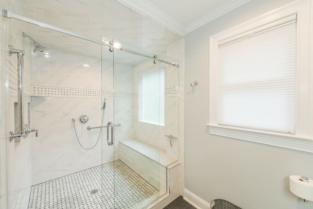 Grey and white master bathroom remodel with farmless shower door, Carrera marble, grab bars, bench seat with handheld shower, basketweave tile floor in Randolph, NJ renovated by JMC Home Improvement Specialists